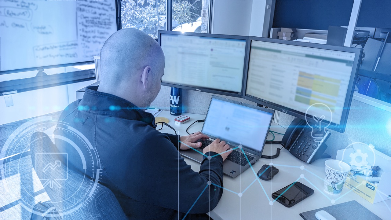 Agent working at a dual-monitor setup in an office, with digital graphics overlay symbolizing data analysis and cyber security.