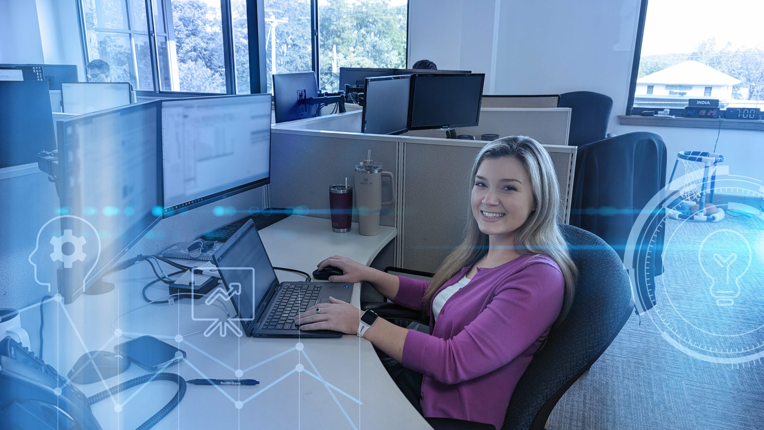 Cyber broker sits at desk in office cubicle, using laptop and dual monitors to review Cyber Insurance premiums.
