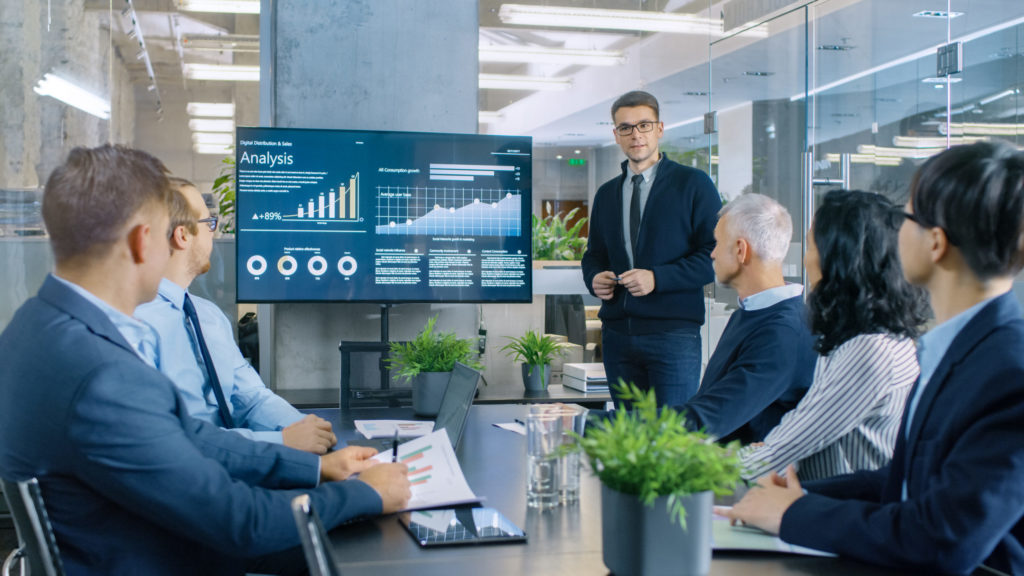Group of colleagues in a meeting view risk analysis on a display screen. 