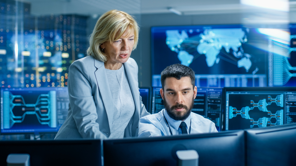  Female business executive and male IT professional investigate data breach via computer.
