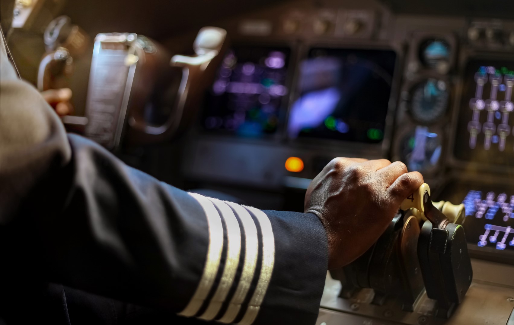 Airline pilot operates complicated, computerized console in cockpit, vulnerable to contingent bodily injury cyber attacks.