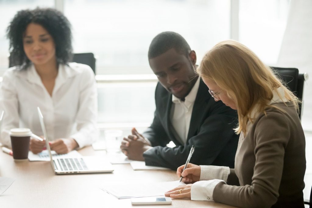 Diverse group of executives discusses cyber security plan and company cyber insurance policies at a conference table. 