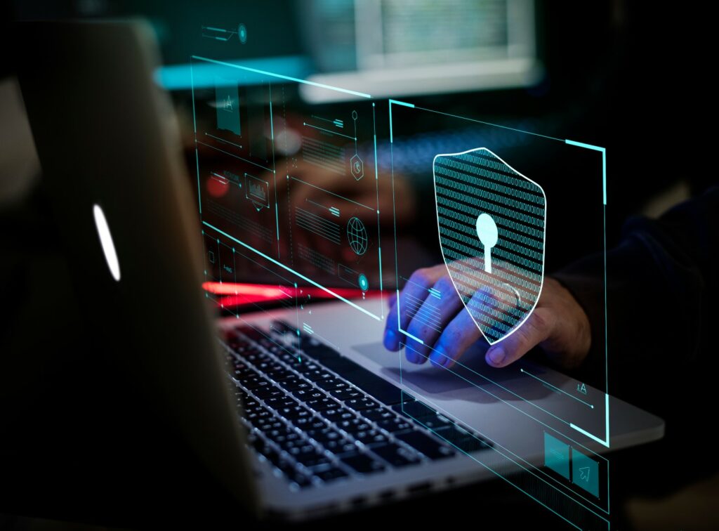 Hacker types on laptop computer keyboard, overlaid with digital security icon, illustrating cyber crime.