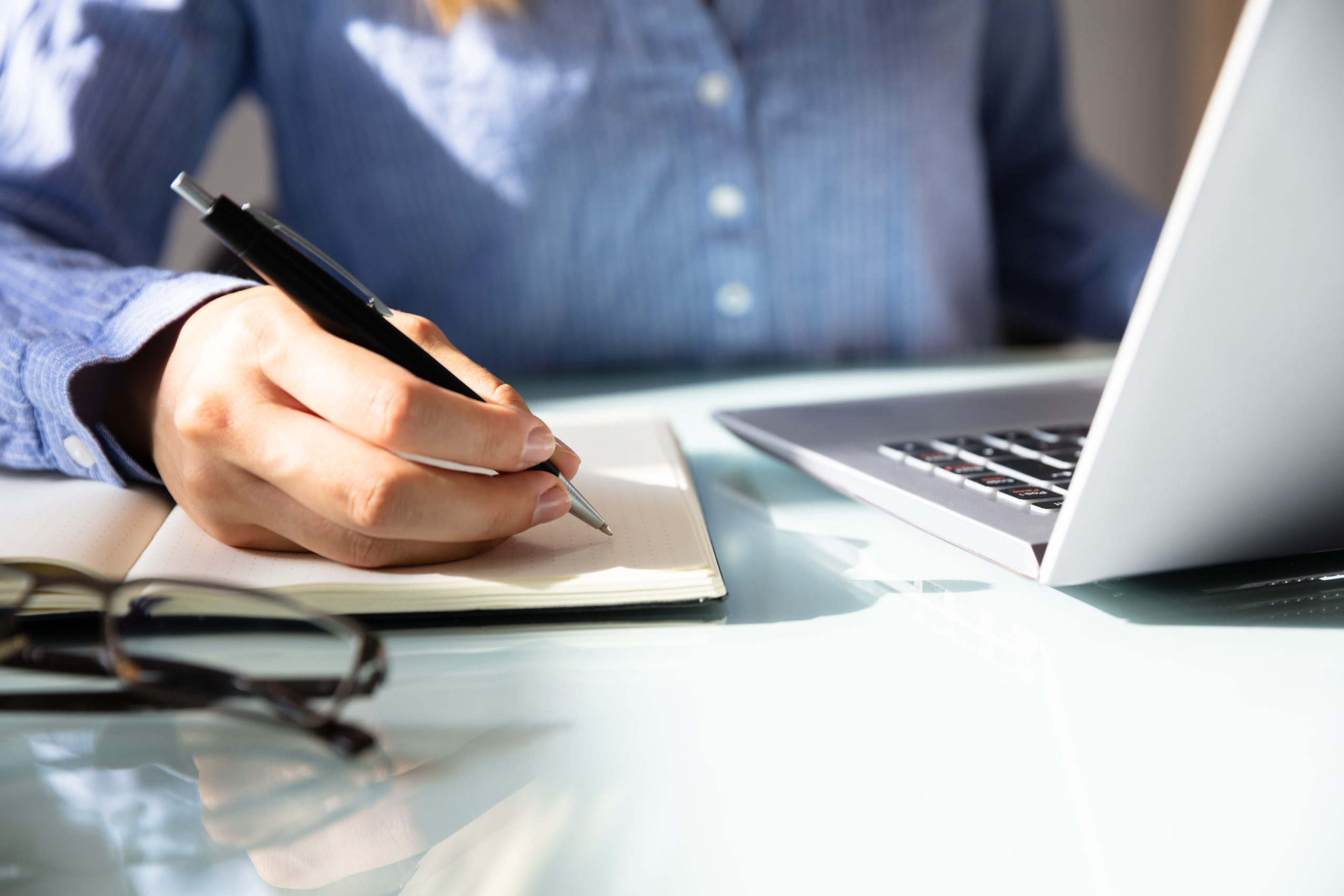 Closeup of businesswoman’s hand taking notes next to a computer