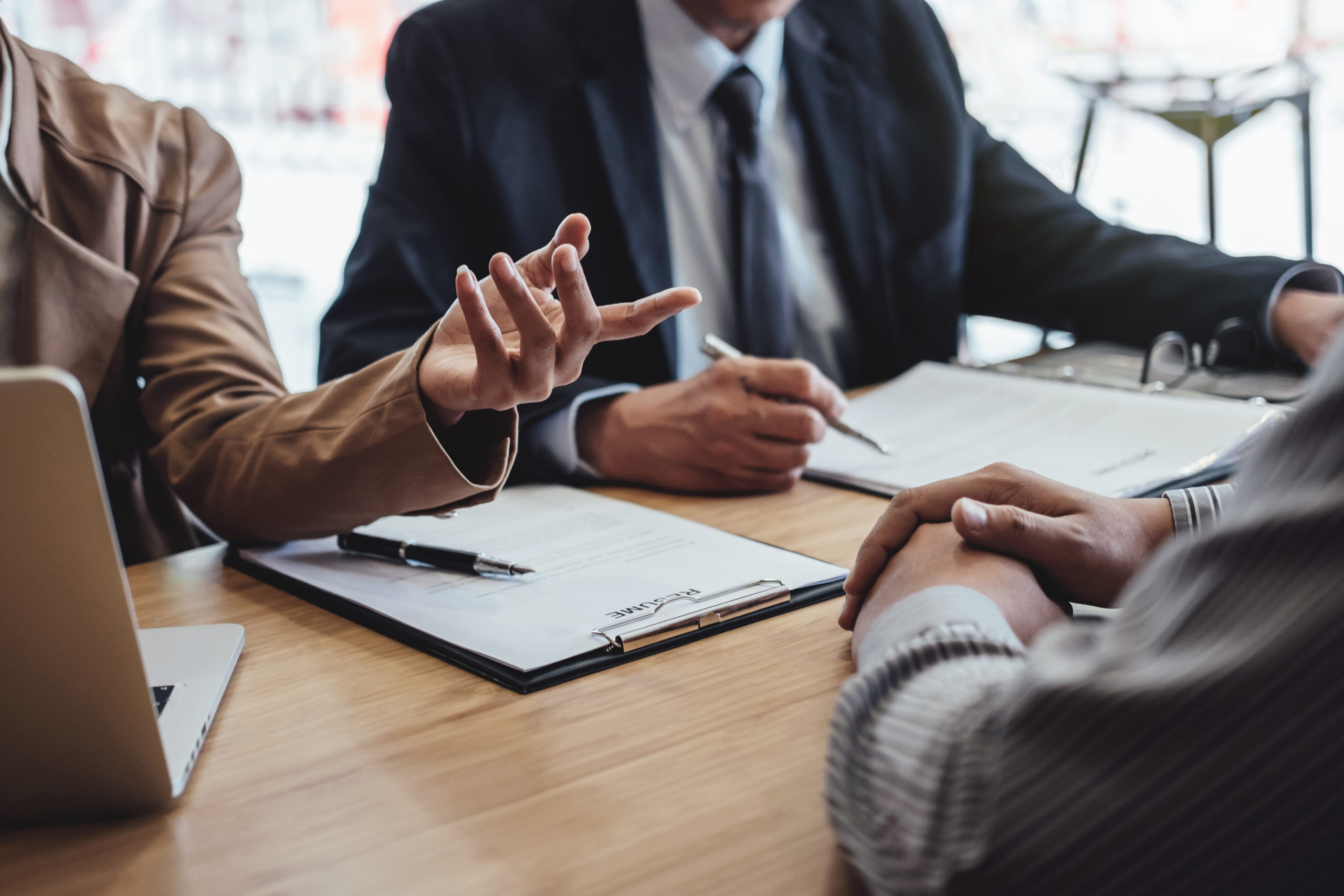  Three businesspeople discuss what Directors and Officers insurance covers at table with notebooks and laptop computer.