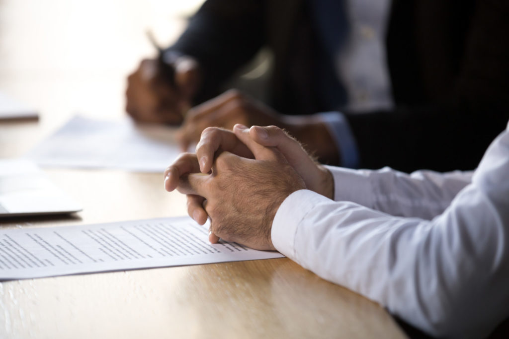  Businessman places folded hands on EPL insurance policy on conference table as broker with pen in hand explains EPL coverage.