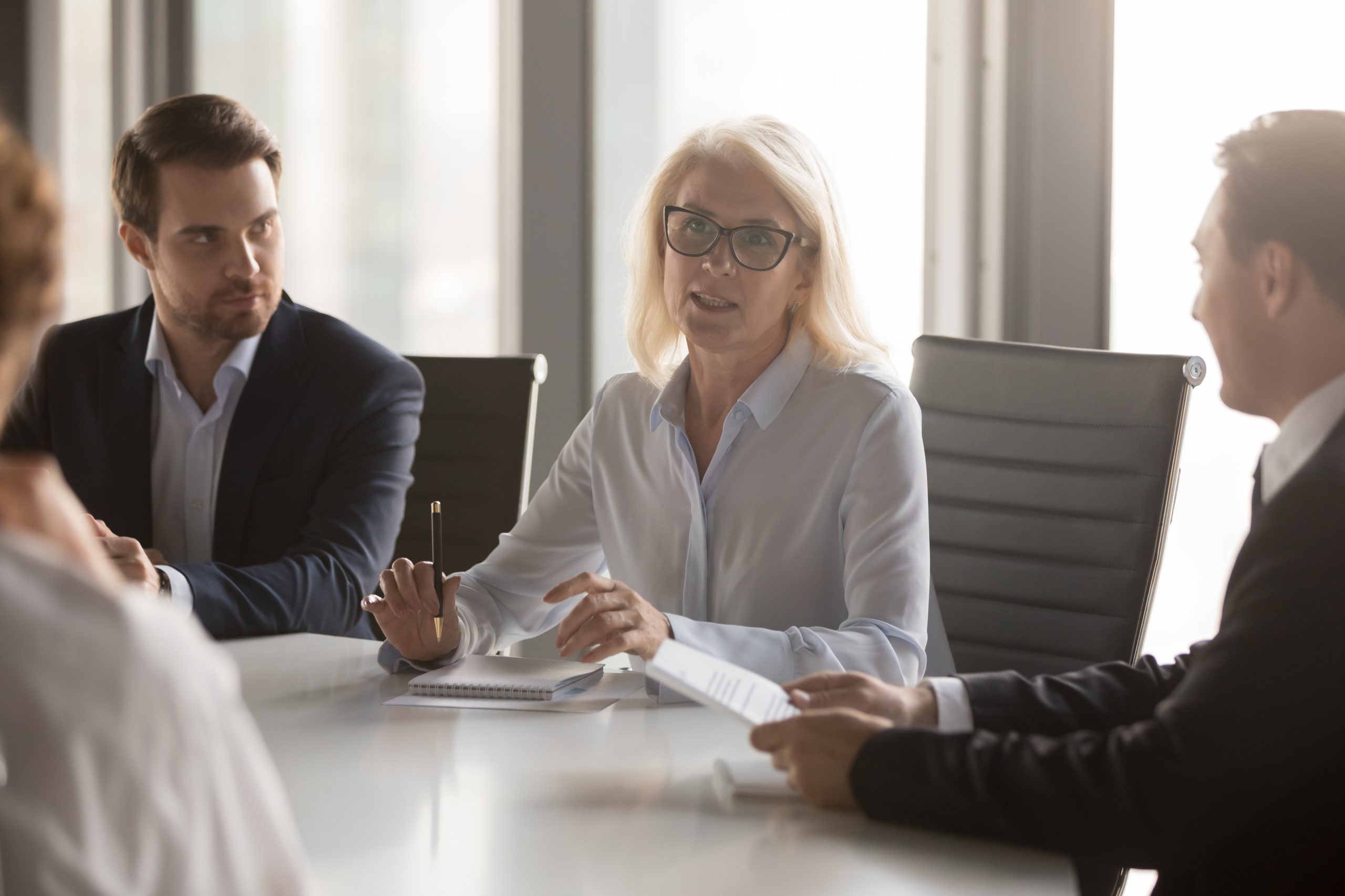  Businesswoman speaks about what goes into a Directors and Officers policy at conference table as three male colleagues listen.