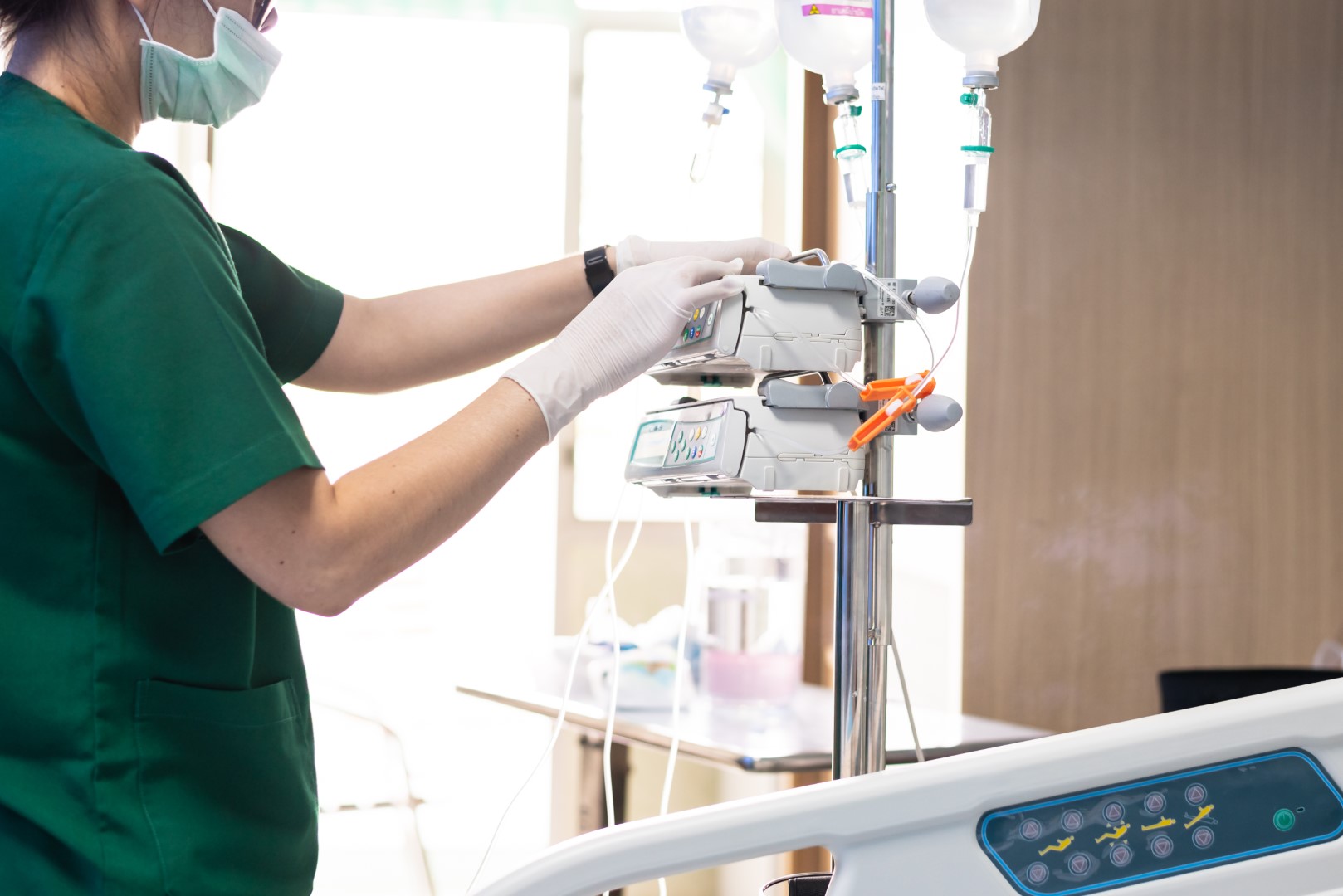 Masked nurse adjusts infusion pump, a connected device vulnerable to contingent bodily injury cyber attack.