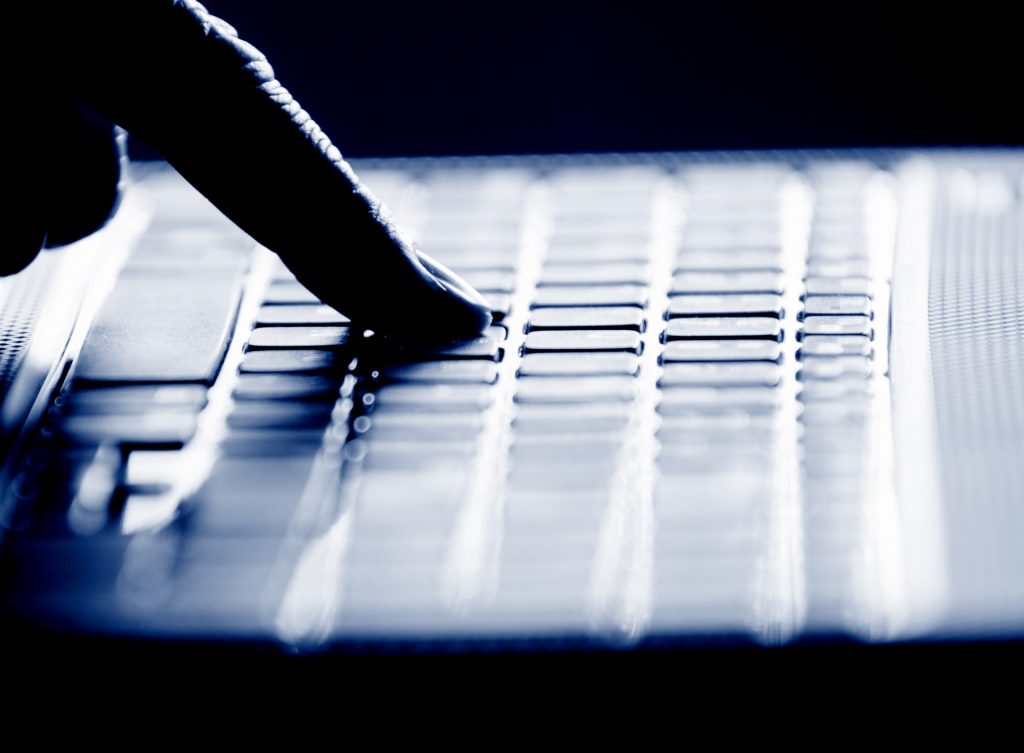 Close up of the silhouette of a finger as it types on a keyboard.