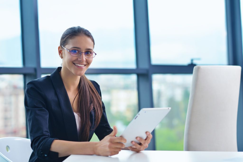 Insurance broker sits at table holding her tablet computer, preparing cyber extortion coverage quote for client. 