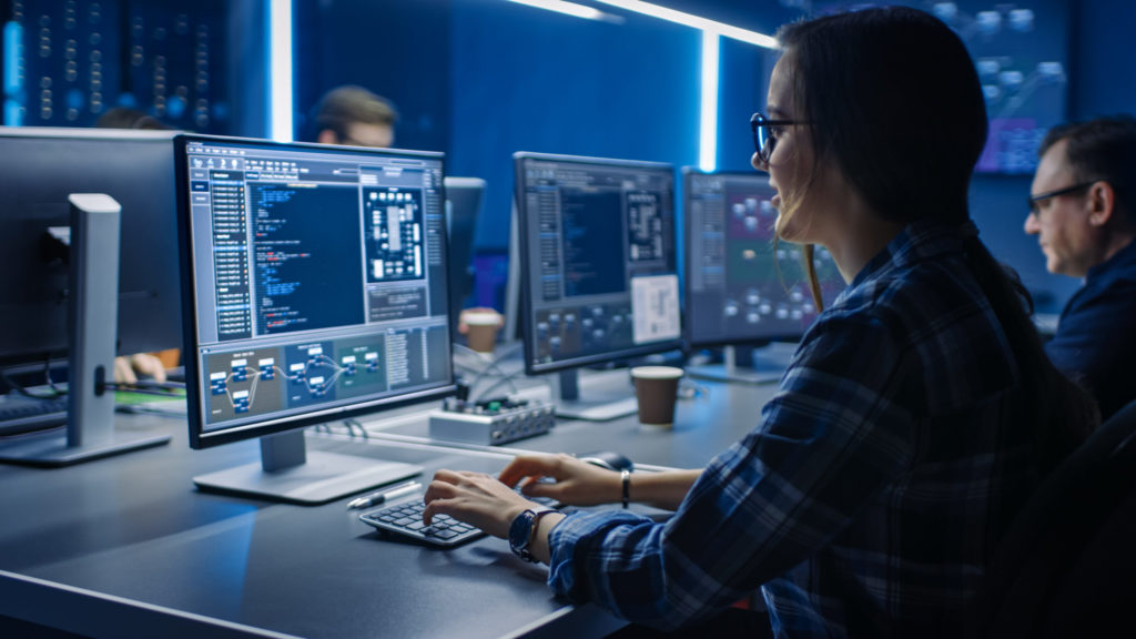 Cyber security professional sits in front of a monitor in a room with blue lights. 