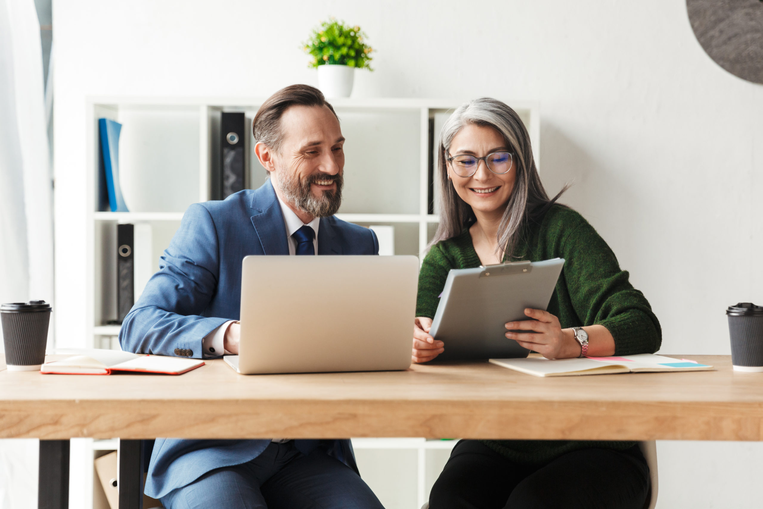 Adults smiling colleagues talking while working with laptop and documents in office