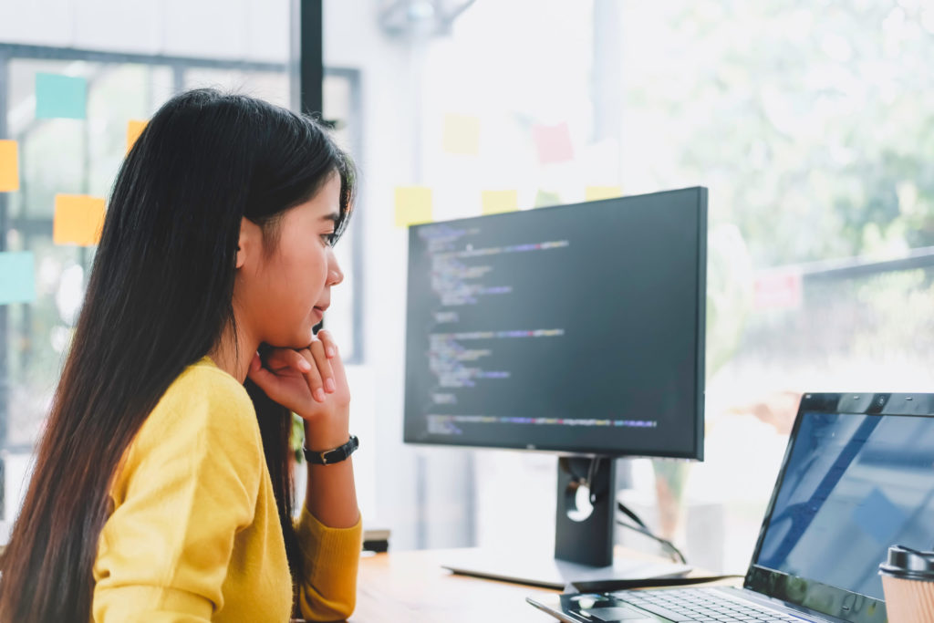 Young female IT professional reviews security code on a computer screen. 