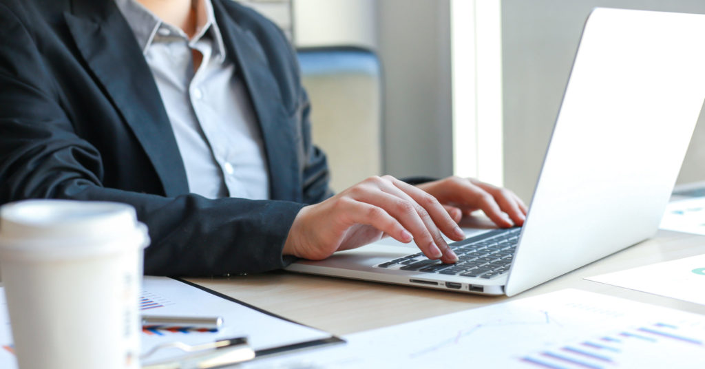 Businessperson in black jacket working on computer researching cyber insurance market.