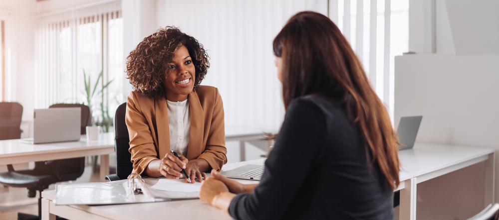 Smiling female broker offers Cyber Insurance policy to businesswoman. 