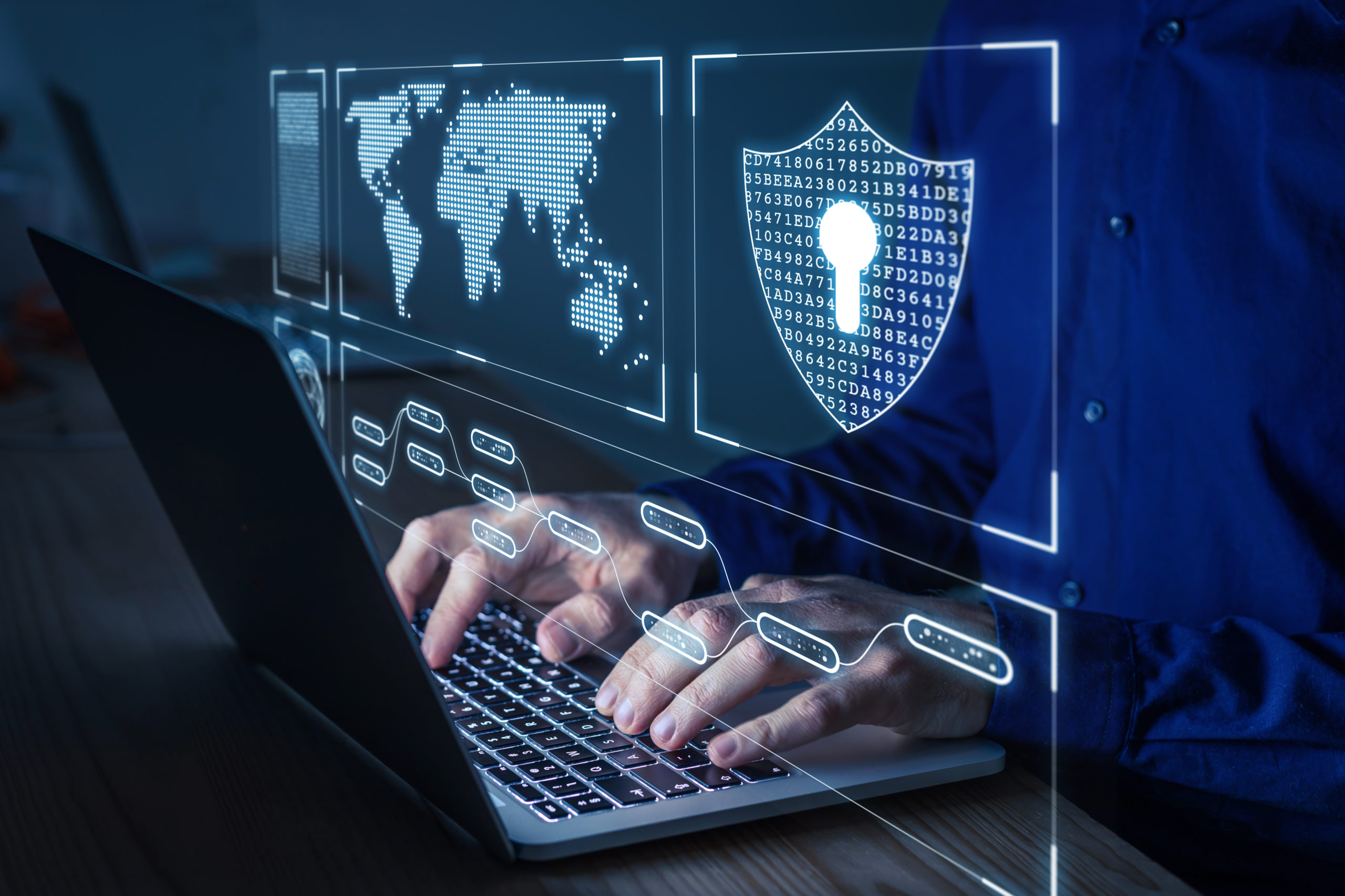 Man types on laptop computer keyboard, holographic world map and security icon visible, suggesting cyber security.