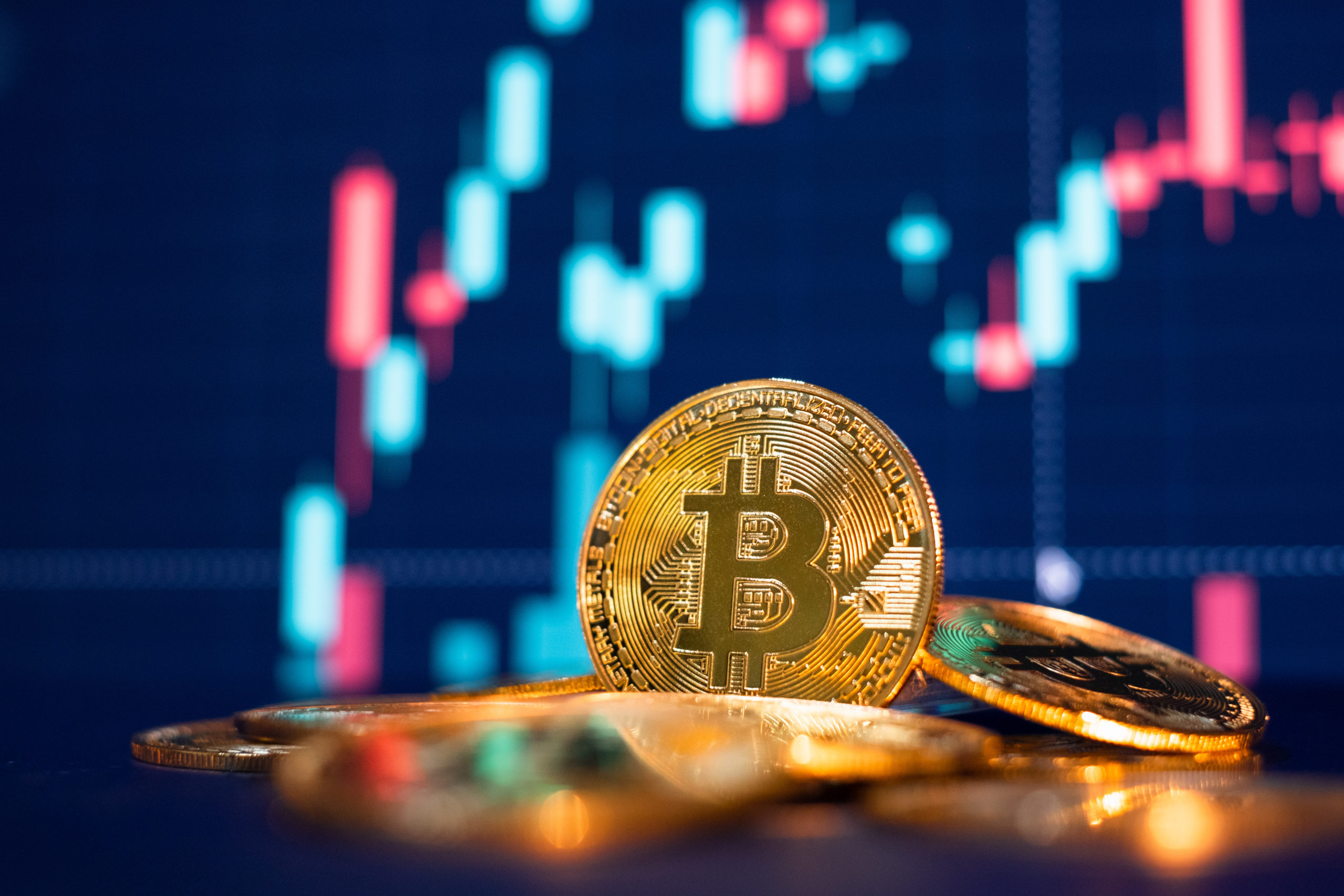  Pile of golden, physical Bitcoins on reflective surface, blurred, illuminated chart behind shows cryptocurrency price rising. 