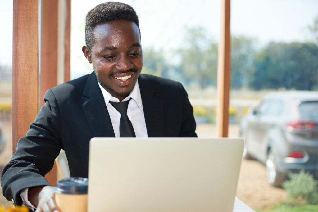  Insurance broker smiles as he sits at desk and uses laptop computer to review Cyber Insurance policies for his clients.