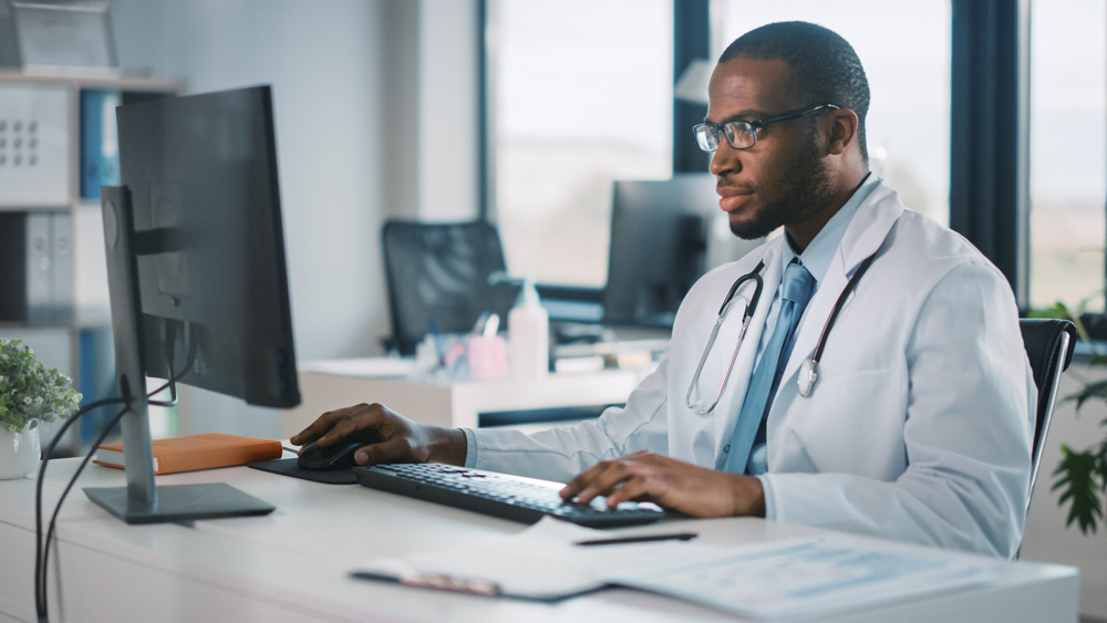 Doctor sits at desktop computer in medical office, reviewing configuration of pixel tools on his website. 