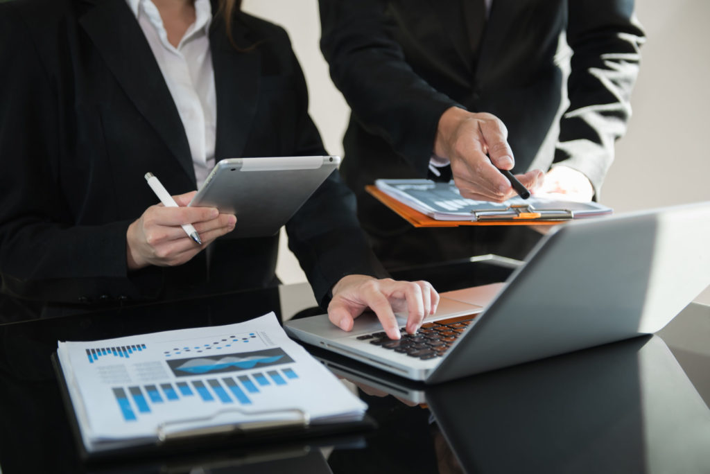 Colleagues review financial data using a tablet and a computer. 