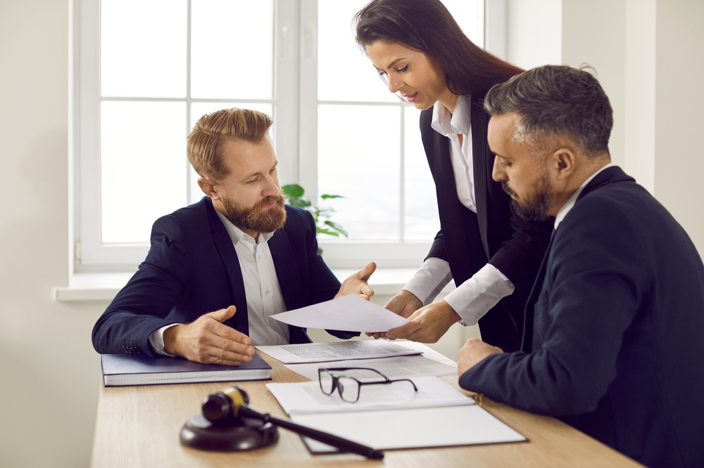  Female lawyer explains legal documents to two businessmen facing a tech E&O lawsuit. 