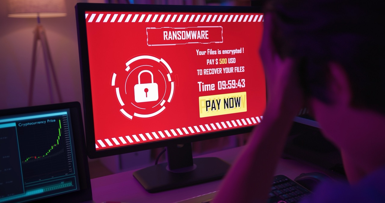 Businessman holds head in hands as his computer monitor displays demand from ransomware gang. 