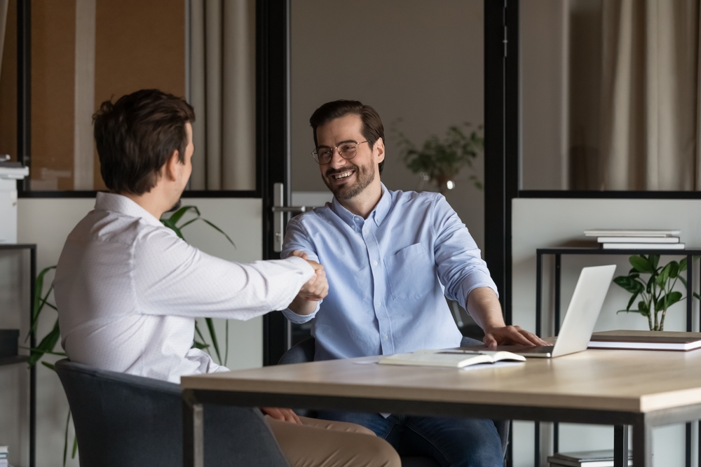  Business client shakes hands with insurance broker after receiving advice on how to lower Cyber Insurance costs. 