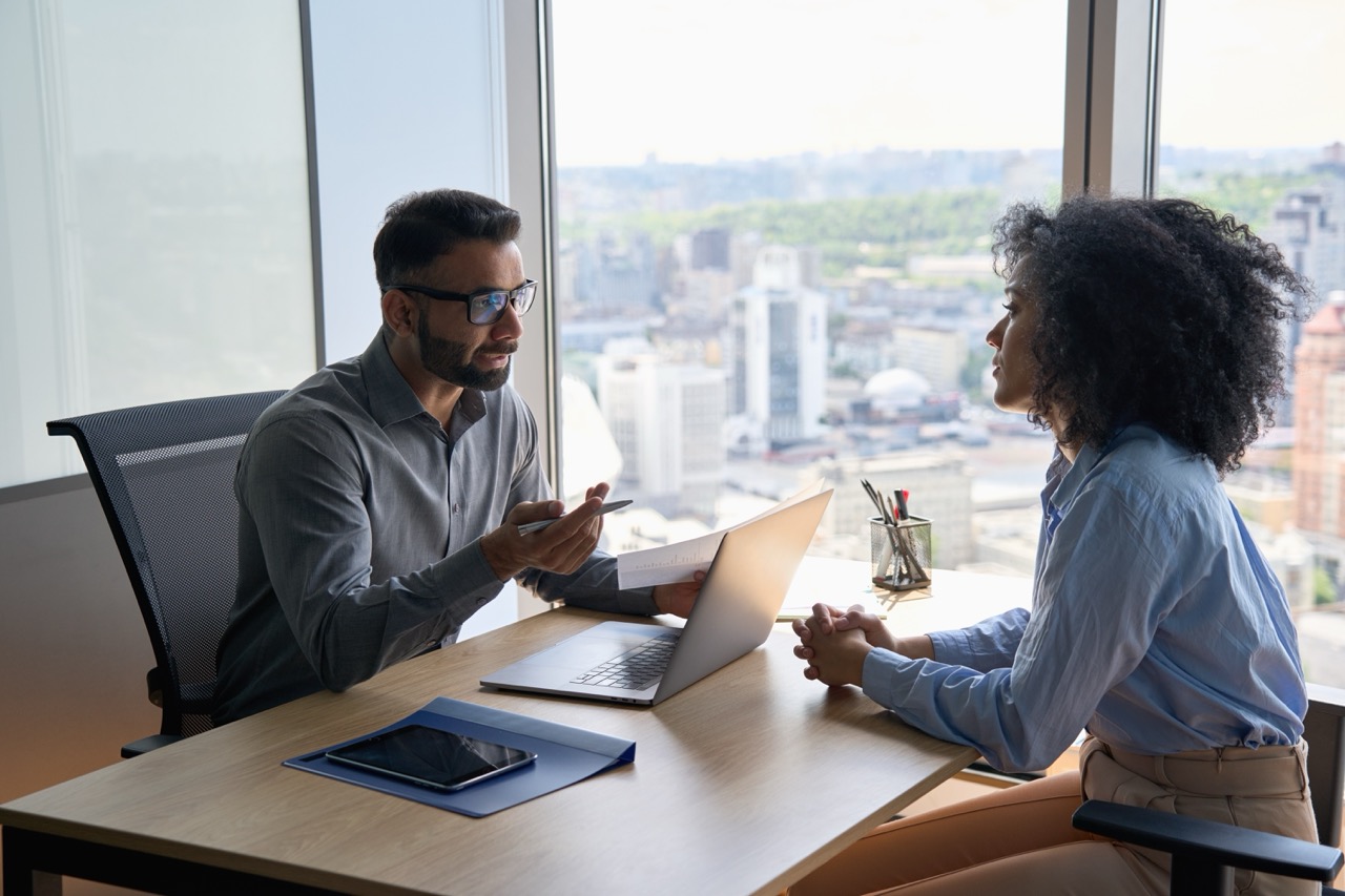 Employer sits at desk with laptop computer, across from employee, discussing HR issue after consulting with EPL Insurance carrier.