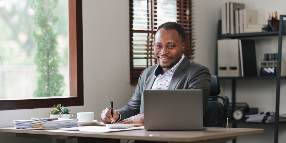 A Cyber Insurance broker sits at a desk with a laptop computer, signing with a fountain pen a paper policy that includes bricking coverage.