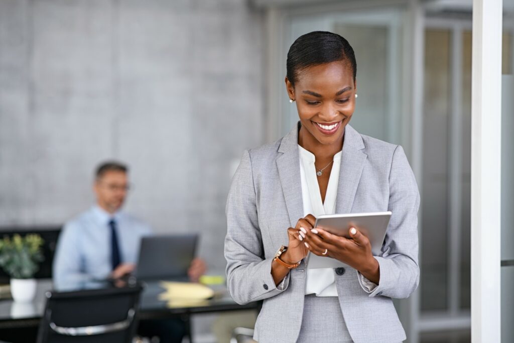 Executive in financial services company smiles as she stands reviewing cyber security requirements on tablet computer.