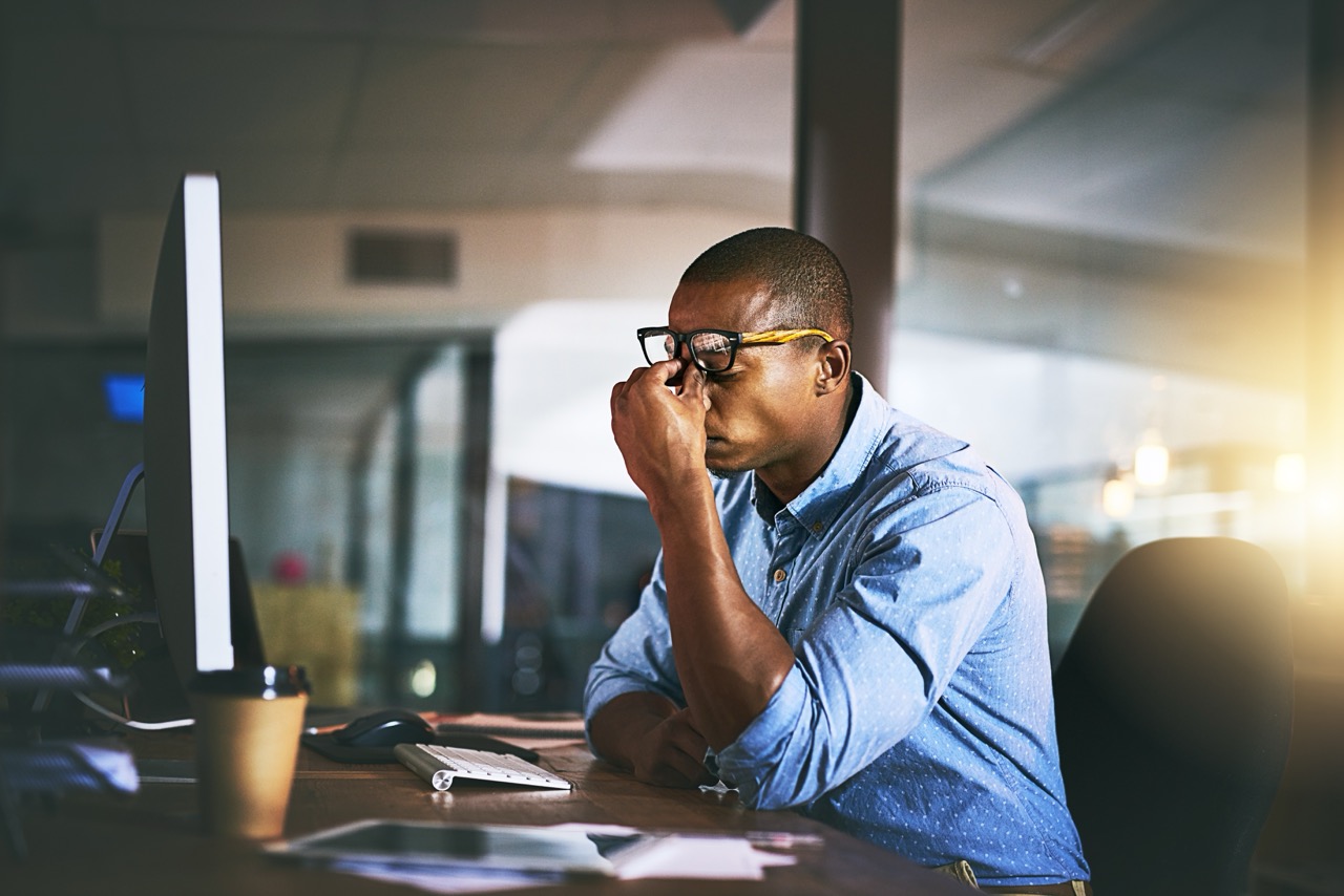 Businessman rubs the bridge of his nose in frustration as his computer is unresponsive during CrowdStrike attack. 