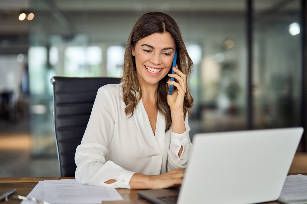 Smiling insurance broker updates client’s contract via phone to cover new D&O risks in 2025.
