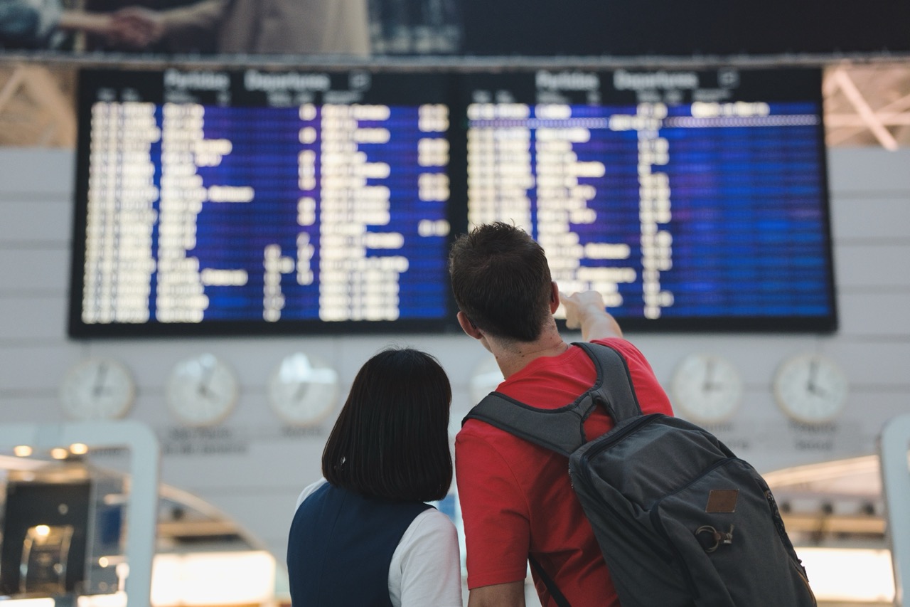 Woman and man in airport look at flight status board, seeing if their flight is canceled in wake of CrowdStrike attack. 
