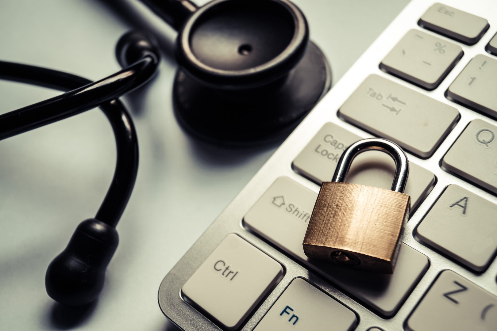 Stethoscope next to computer keyboard on which padlock rests, illustrating concept of preventing healthcare data breaches.