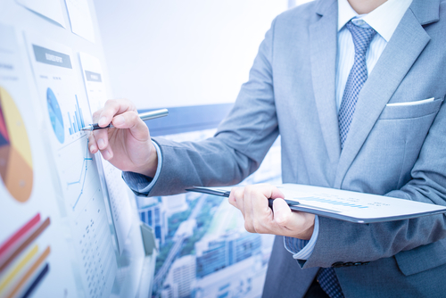 Man in suit writes on a whiteboard, where graphs are featured.
