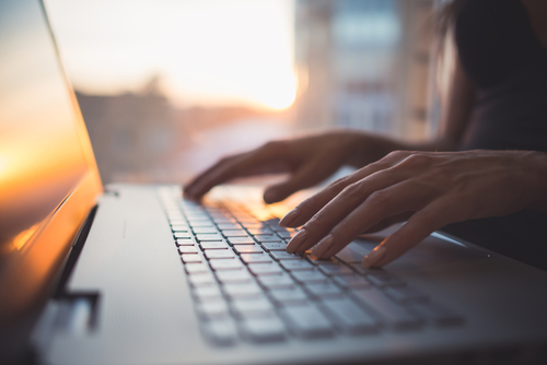 Woman at home typing on laptop with sunset light in the background. LSI: ransomware attack, ransomware prevention