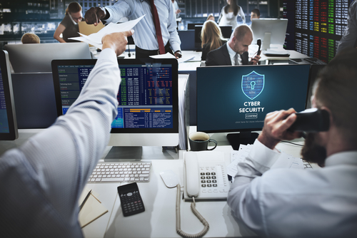 Office with busy workers and computer screen showing cybersecurity firewall.