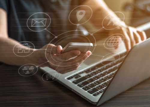 Vector graphic of cyber network concept overlay on closeup of worker using smartphone and typing on a laptop.