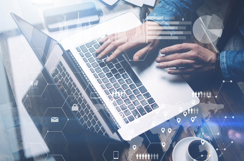 Close up of a man’s hands while he works at a laptop with a cup of coffee next to him. 