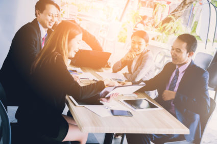 Men and women in business attire review documents at a table outside.