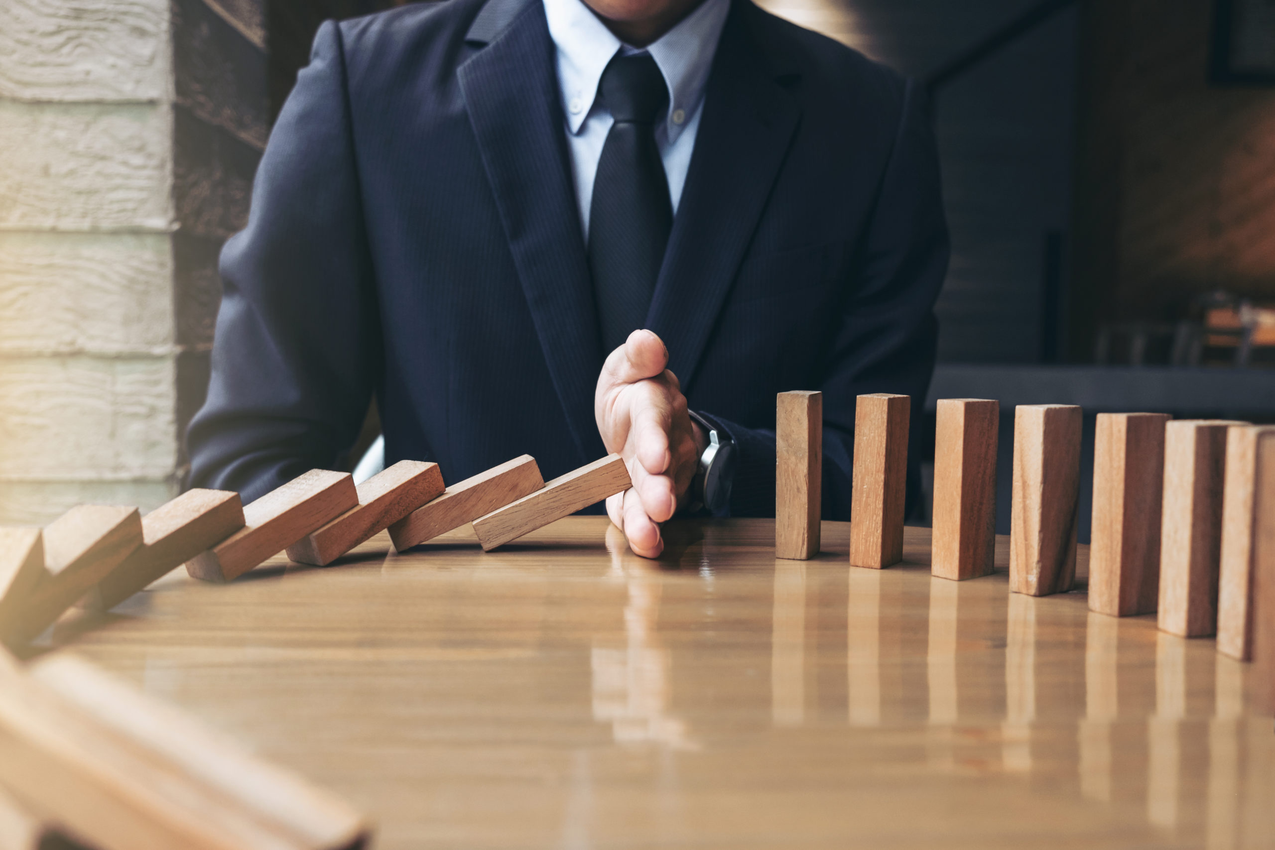Close up of a businessman hand stopping falling wooden dominoes on a desk. Business interruption insurance concept.