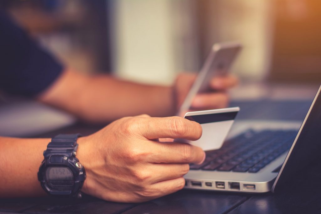 Close up of a credit card being held by a customer as they complete an online purchase on their laptop. 