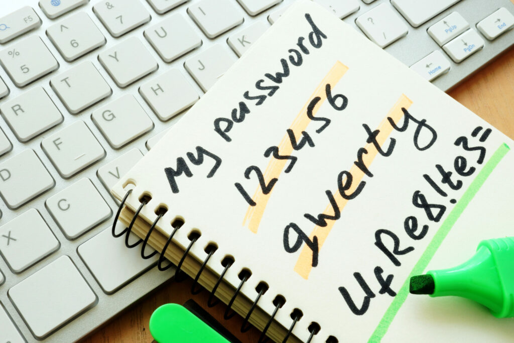 Spiral notebook with two weak passwords and one strong password written in it, next to computer keyboard