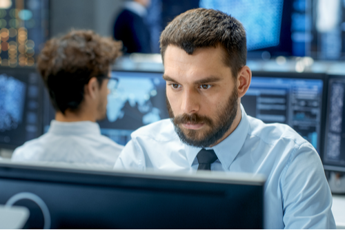 A business professional man sits in front of a desktop computer, working. 